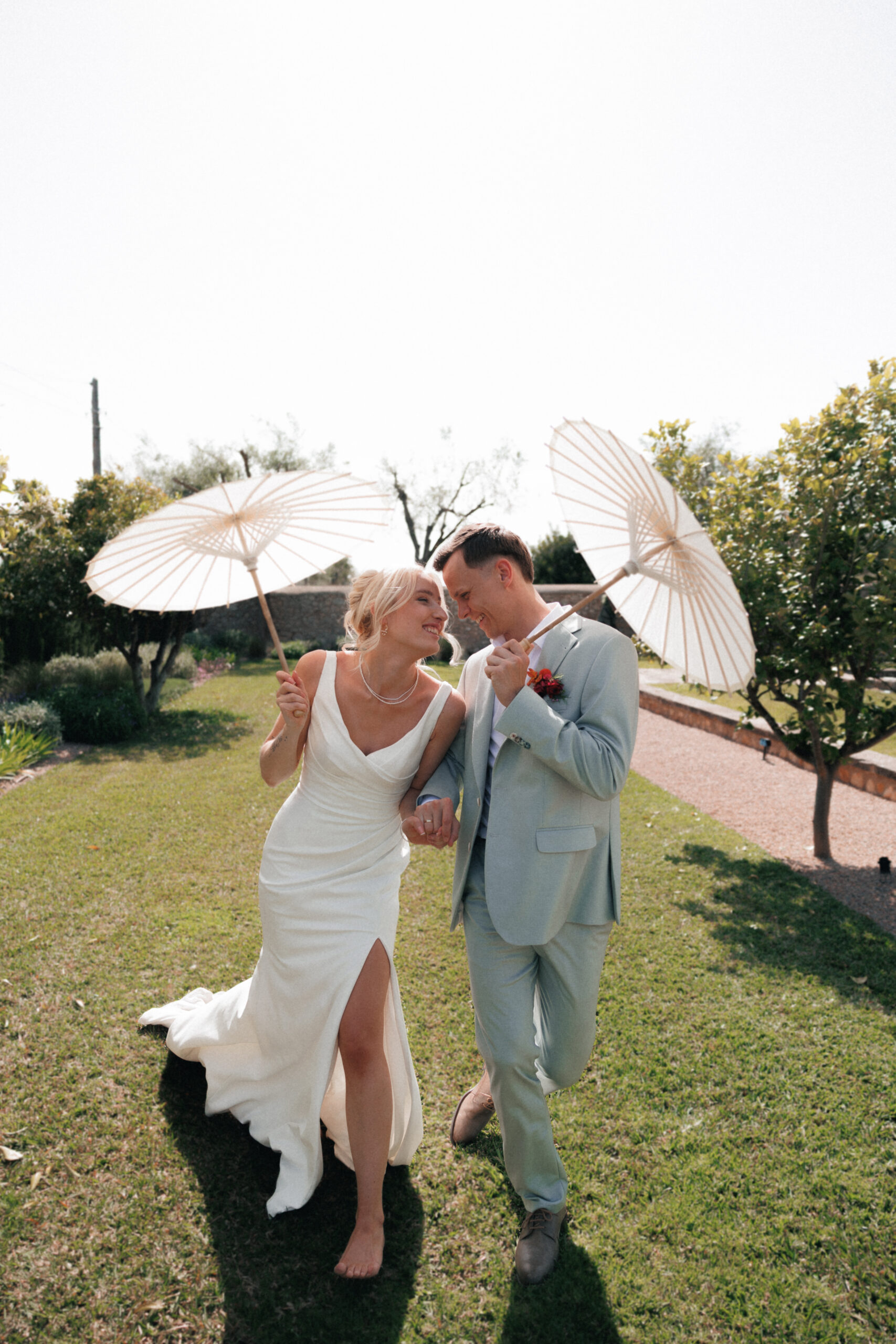Happy bride and groom walking on a meadow with umbrellas during a luxury destination wedding in Europe.