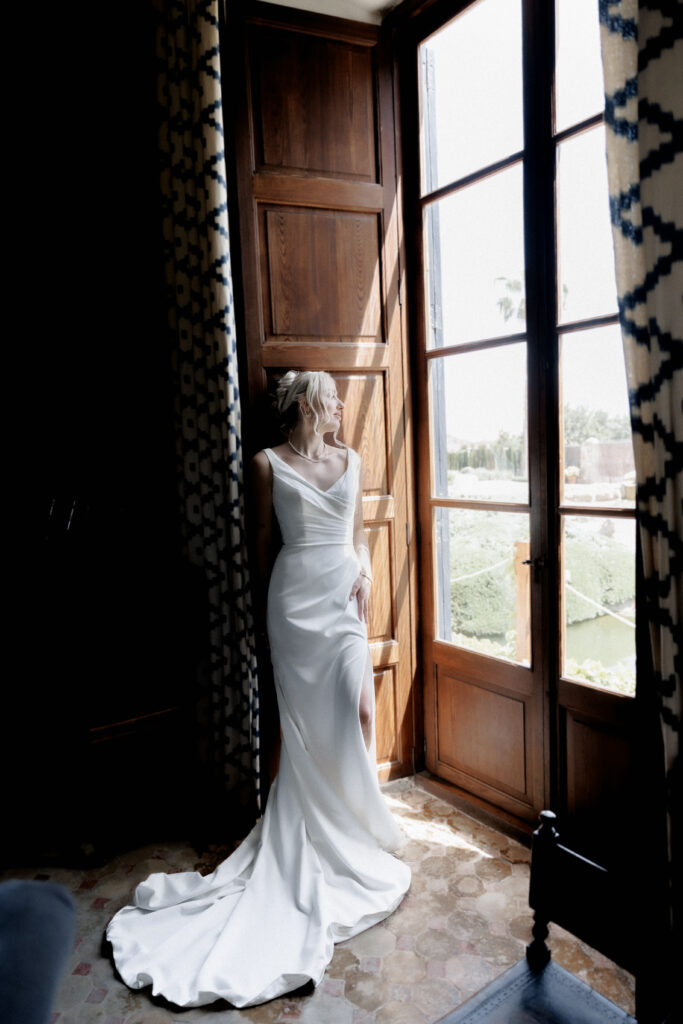 Braut im eleganten Brautkleid am Fenster der Finca Morneta bei natürlichem Tageslicht